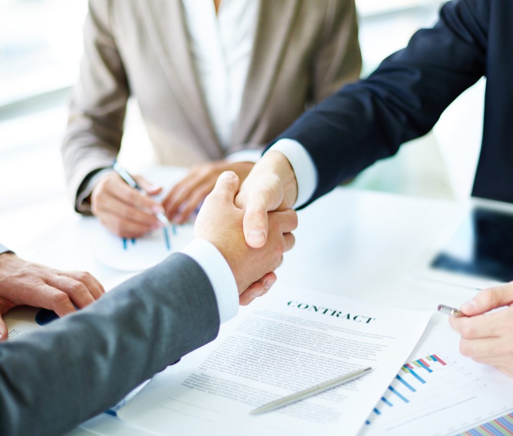 Image of business partners handshaking over business objects on workplace